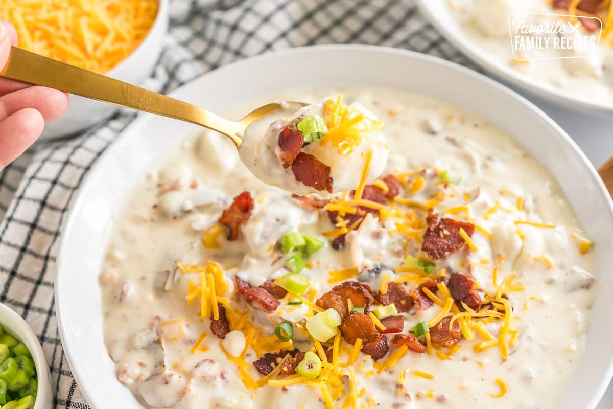 a spoon lifting a bite out of bowl of loaded baked potato soup topped with bacon, cheese, and green onions