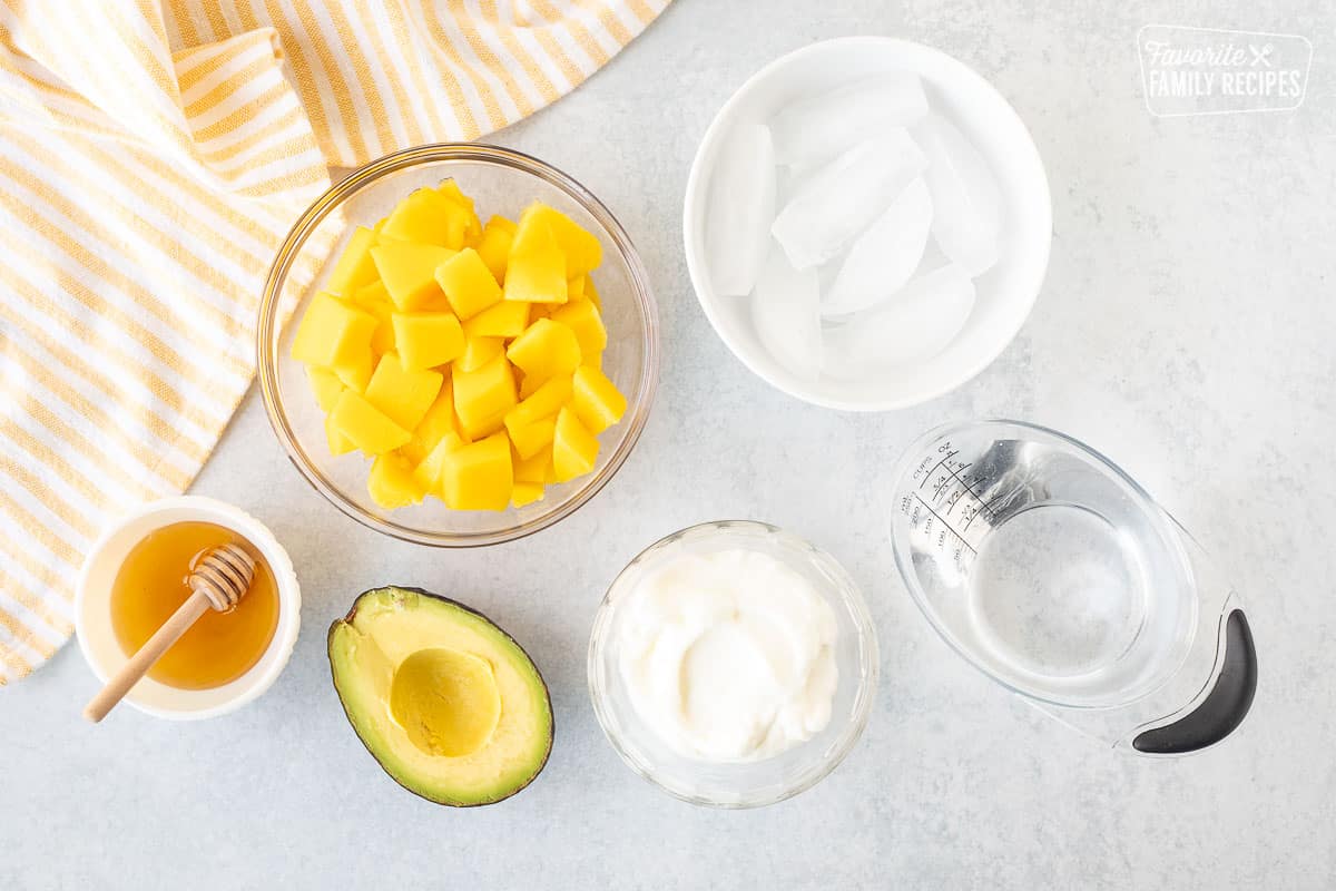 Ingredients to make Mango Avocado Smoothies including sliced mangos, ice, water, greek yogurt, avocado and honey.