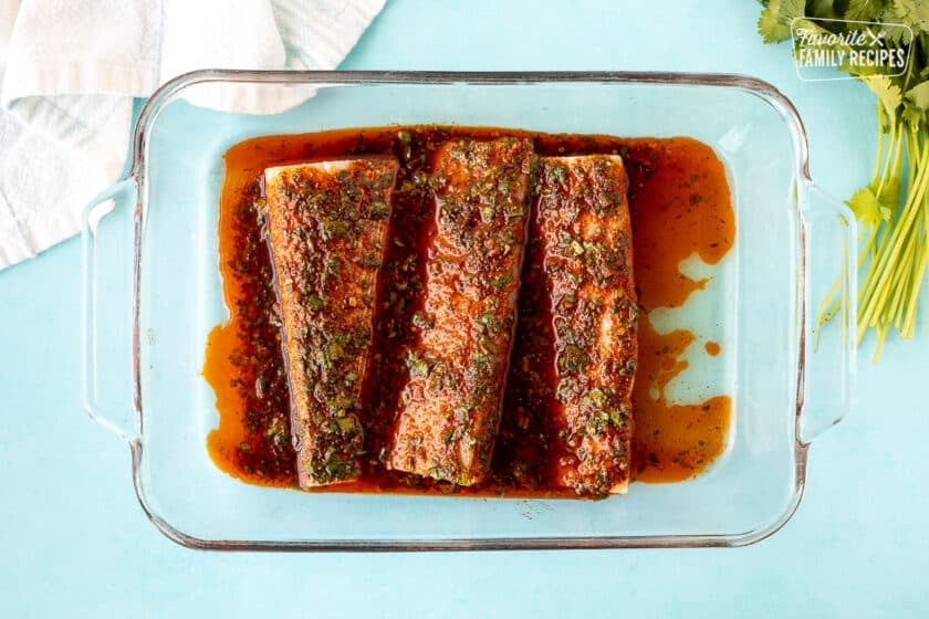 Glass dish with three fillets of mahi mahi and marinade.