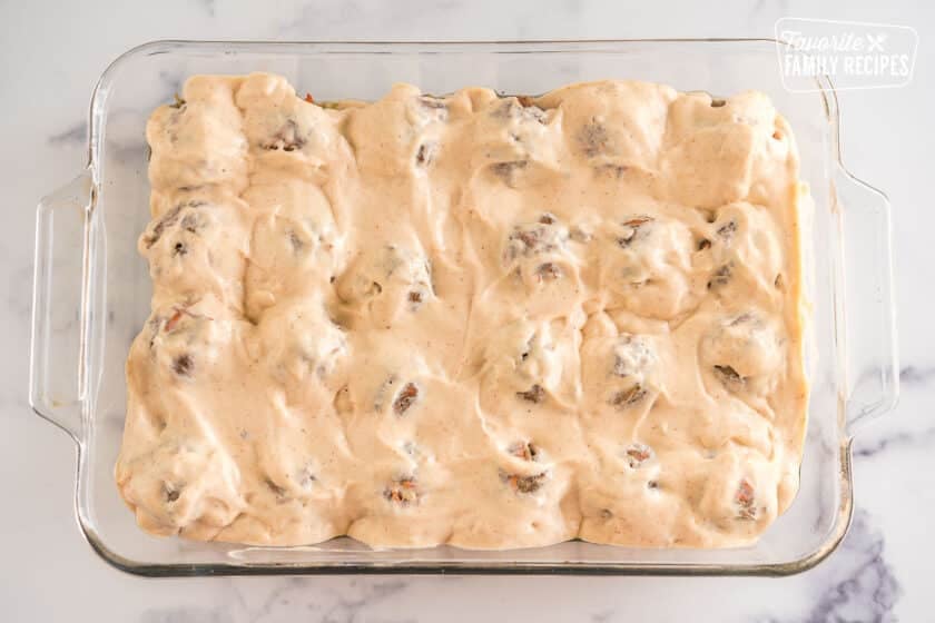 Cream sauce poured over meatballs in a baking dish, before being baked