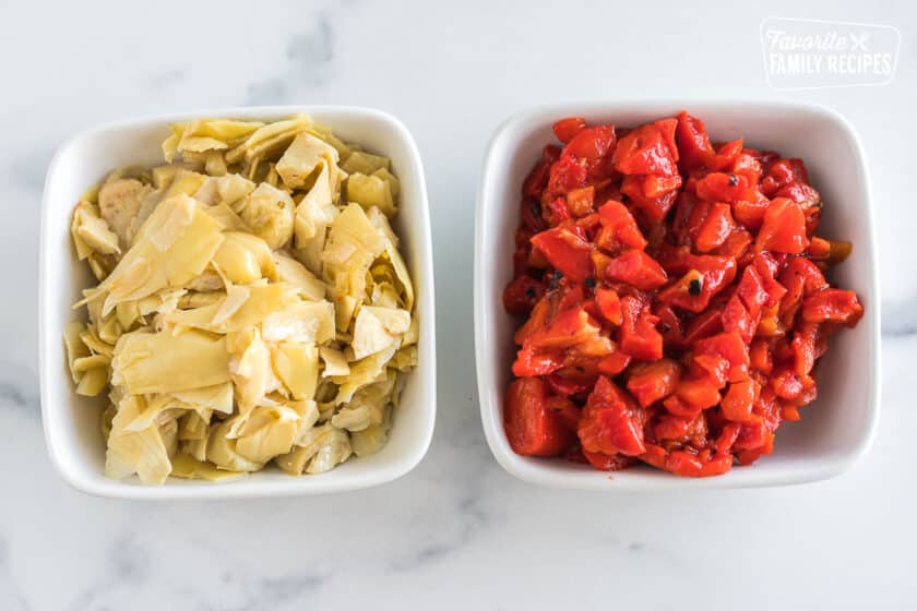 A bowl of chopped artichoke hearts and a bowl of chopped roasted red peppers