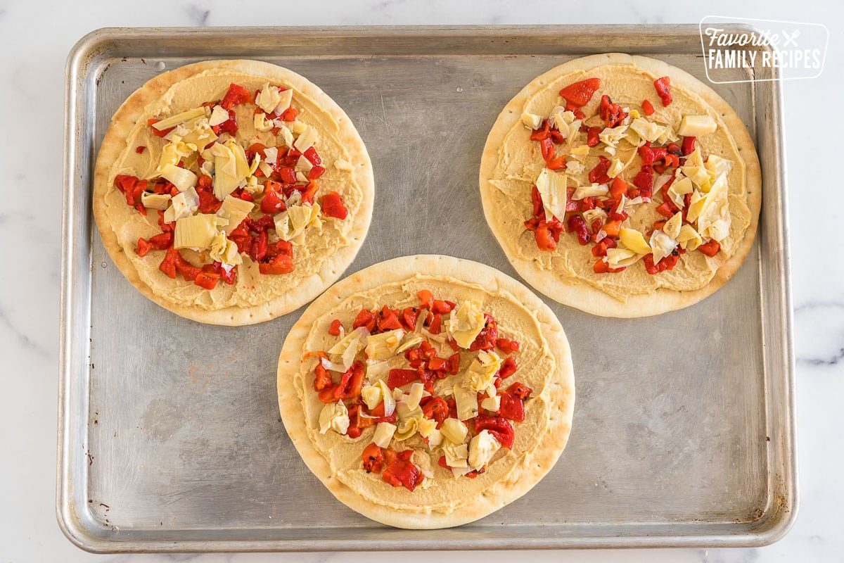 Three pitas topped with hummus, artichokes, and roasted red pepper