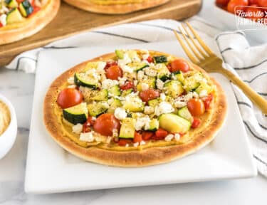 A pita topped with hummus, tomato, feta, zucchini, artichokes, and roasted red pepper