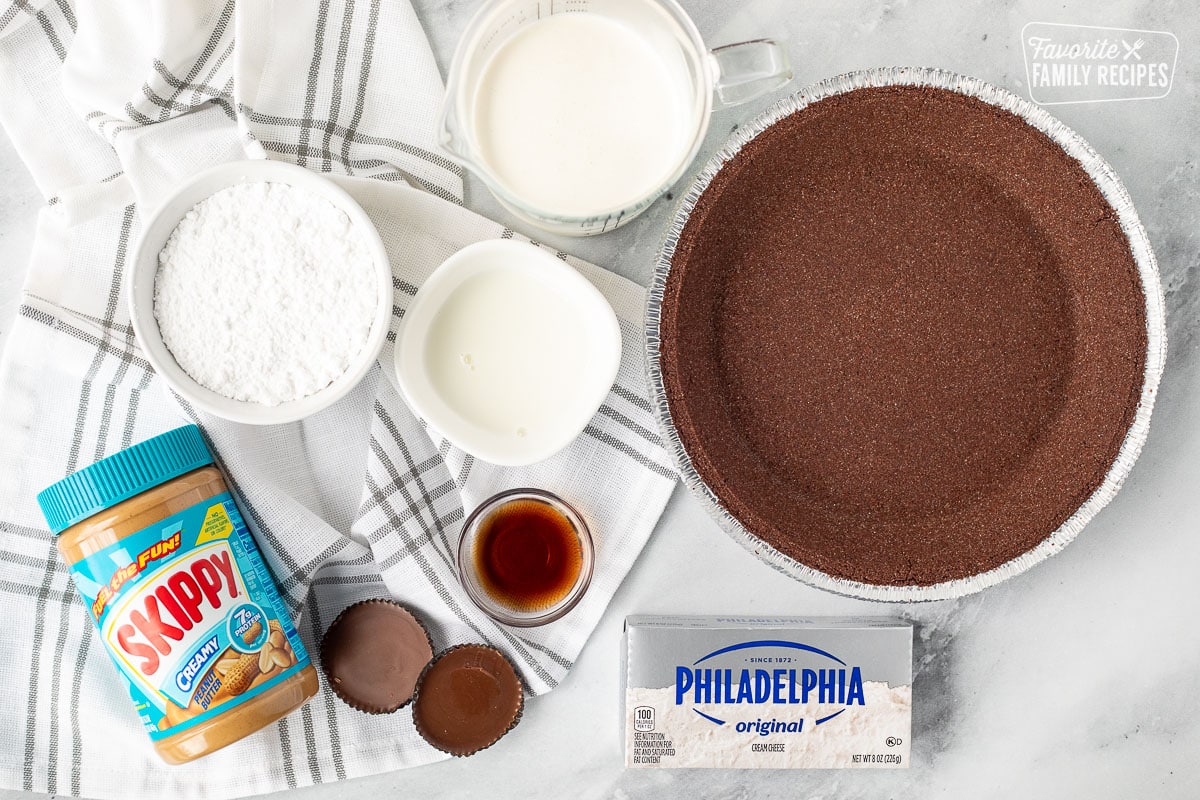 Ingredients to make Peanut Butter Pie including chocolate pie crust, cream cheese, milk, heavy cream, powdered sugar, creamy peanut butter, vanilla and Reese's peanut butter cups.