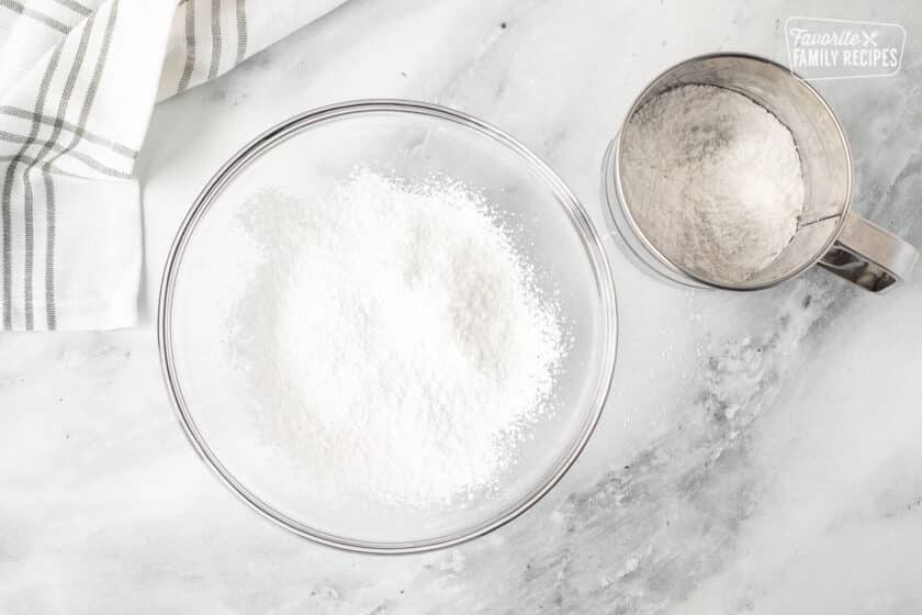 Bowl of sifted powdered sugar next to a sifter.