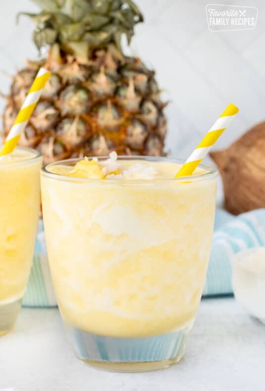 Glass of Pina Colada Smoothie with pineapple and coconut on top and a straw.