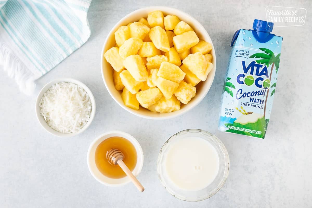 Ingredients to make Pina Colada Smoothies including frozen pineapple, coconut water, coconut, honey and milk.