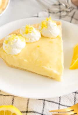A slice of Sour Cream Lemon Pie on a plate topped with whipped cream and lemon zest