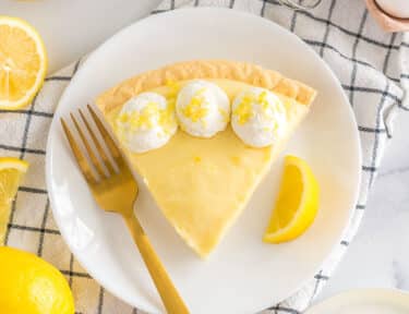 A slice of Sour Cream Lemon Pie on a plate topped with whipped cream and lemon zest