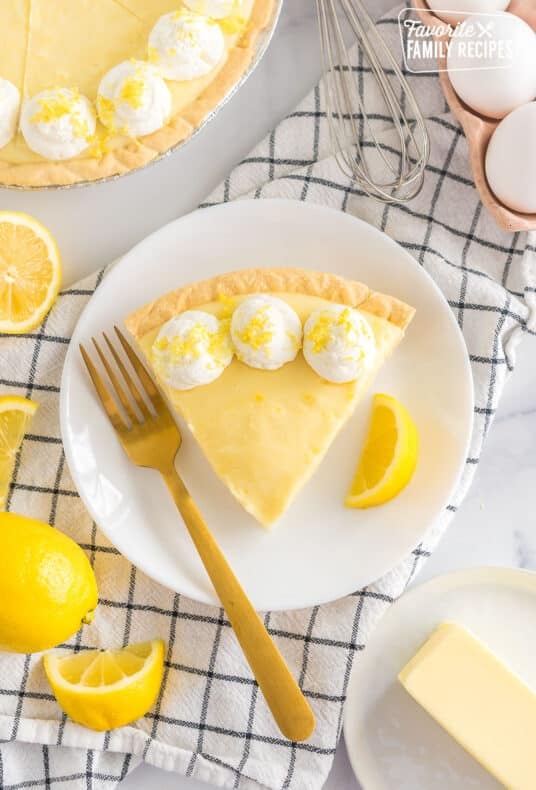 A slice of Sour Cream Lemon Pie on a plate topped with whipped cream and lemon zest