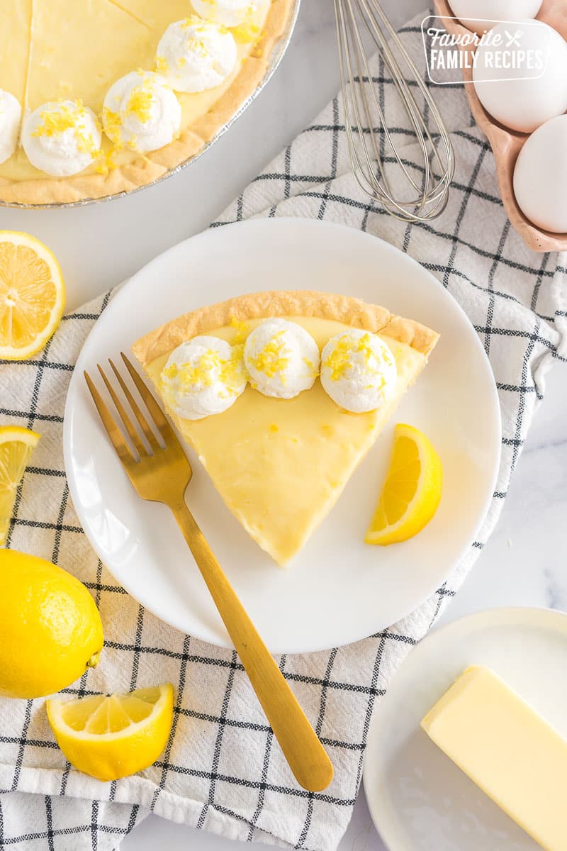 A slice of Sour Cream Lemon Pie on a plate topped with whipped cream and lemon zest