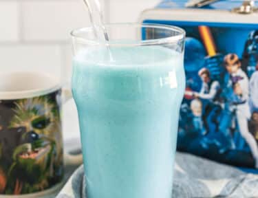 blue milk in a tall glass with a straw in front of a star wars lunchbox and a Chewy mug