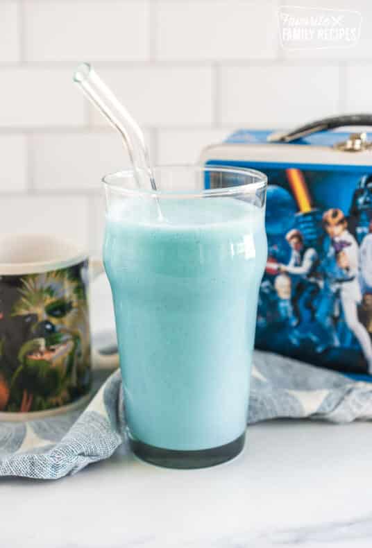 blue milk in a tall glass with a straw in front of a star wars lunchbox and a Chewy mug