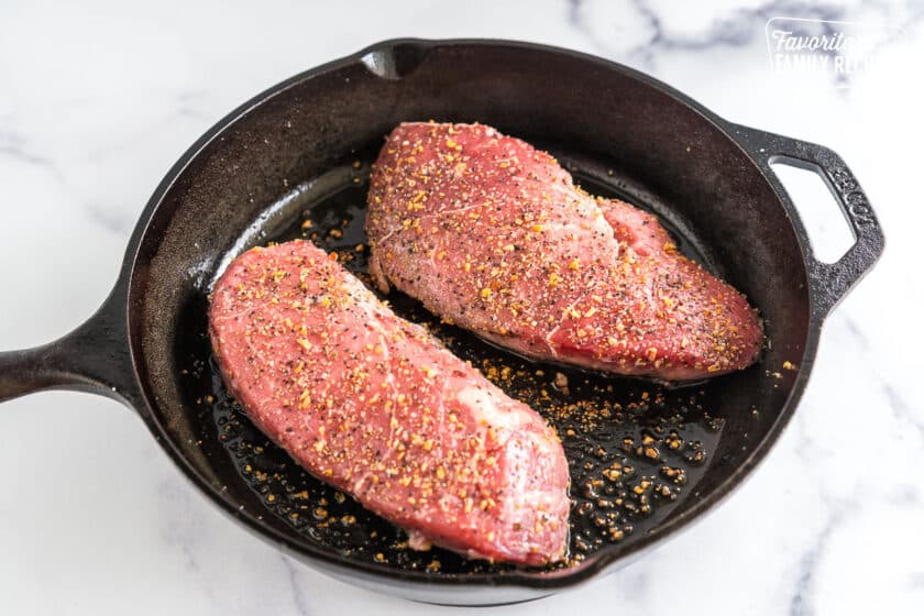 two sirloins seasoned and cooking in a cast iron pan