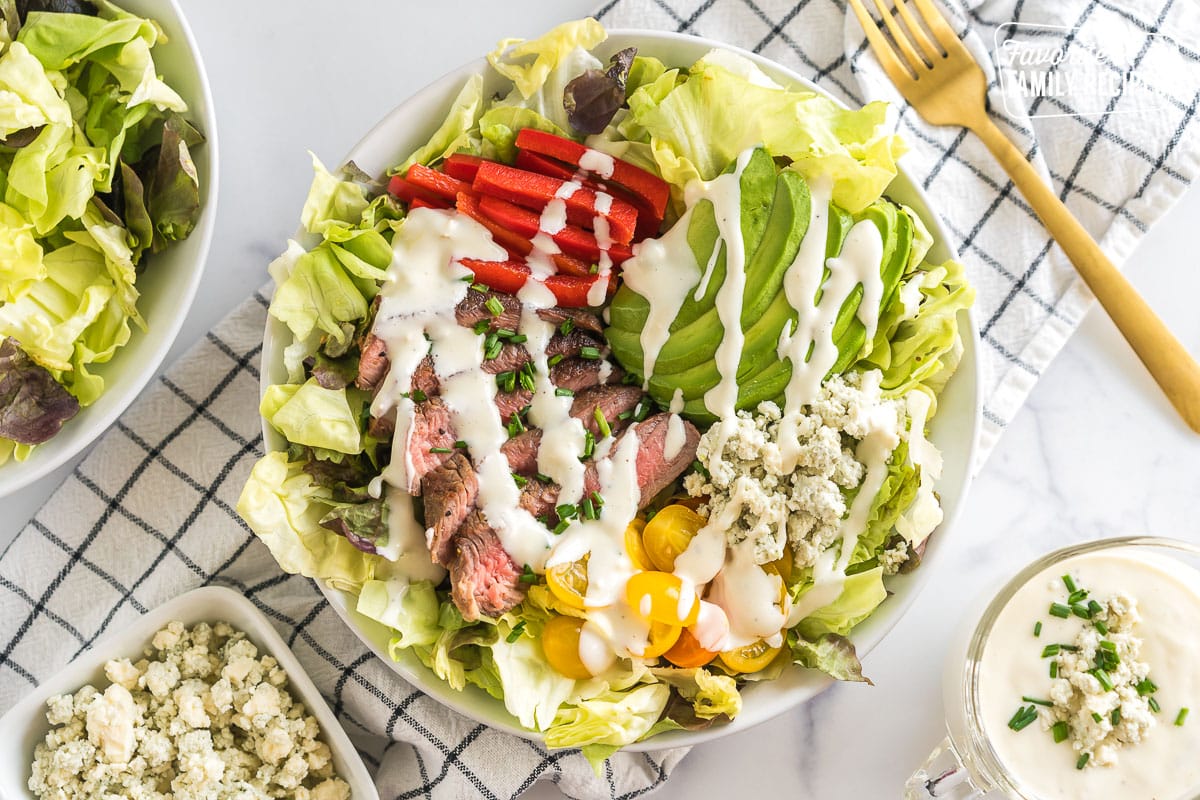 Butter lettuce, tomatoes, blue cheese, avocado, red pepper, and slices of beef in a bowl topped with blue cheese dressing