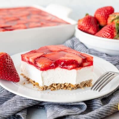 Plate with Strawberry Pretzel Salad with a fork and a fresh strawberry.