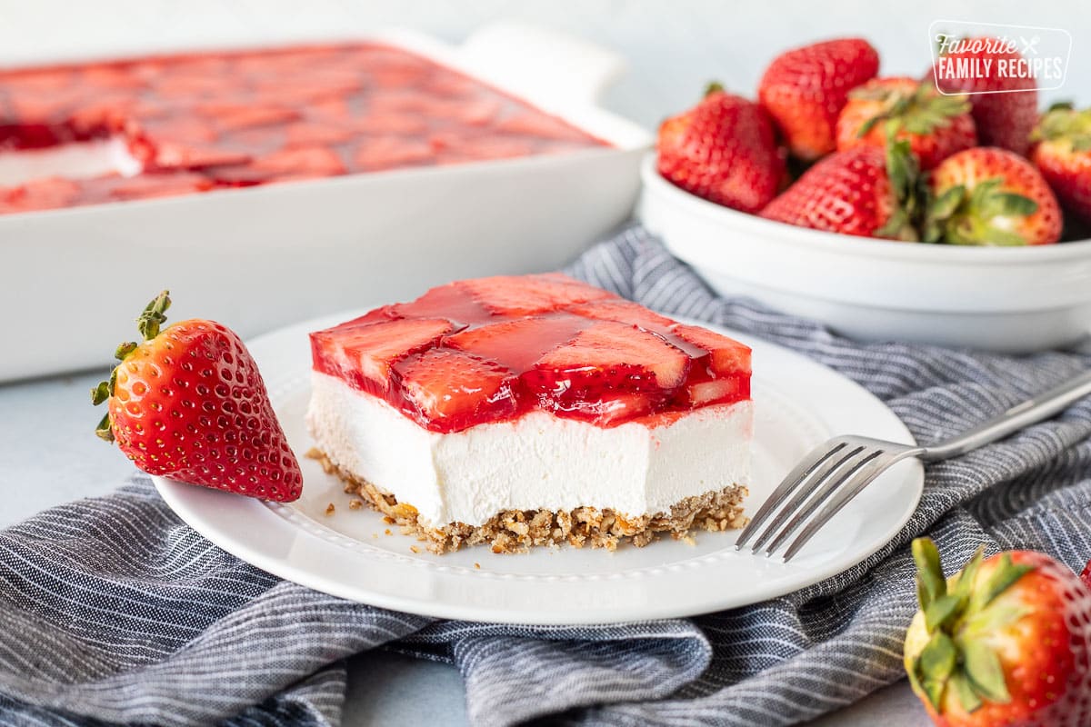 Plate with Strawberry Pretzel Salad with a fork and a fresh strawberry.