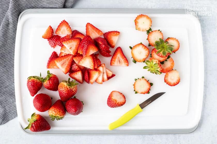 Cutting board with sliced strawberries and a knife.