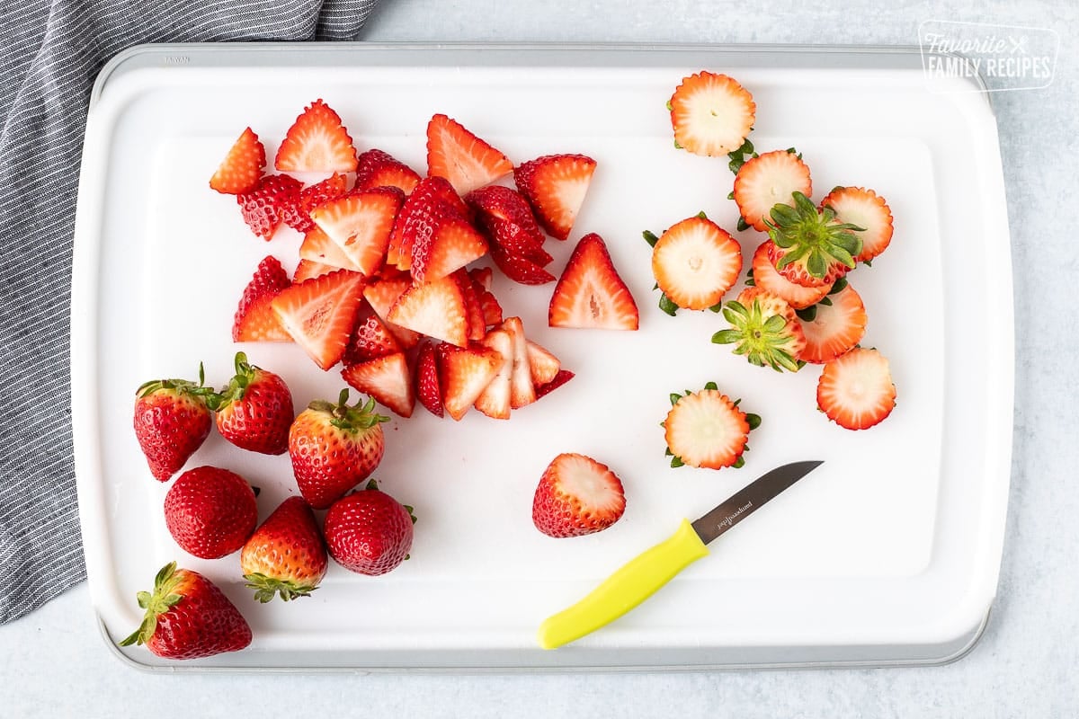 Cutting board with sliced strawberries and a knife.