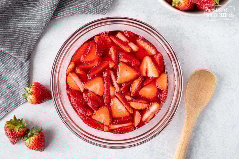 Strawberries in a bowl of strawberry jello. Wooden spoon on the side.