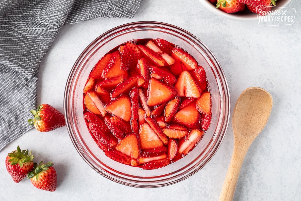 Strawberries in a bowl of strawberry jello. Wooden spoon on the side.