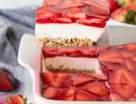 Slice of Strawberry Pretzel Salad on a spatula above dish of Strawberry Pretzel Salad.