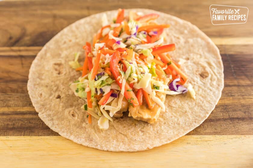 a whole wheat tortilla topped with peanut chicken and thai slaw