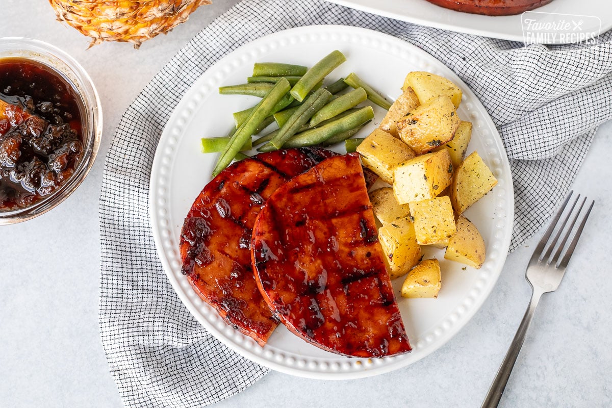 Plate with two halved sweet teriyaki ham steaks, potatoes and green beans.