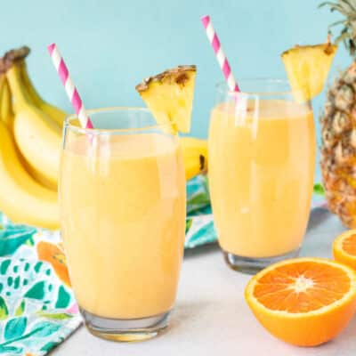 Two glasses of Tropical Banana Smoothies with fresh pineapple and straws.