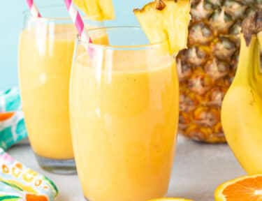 Two glasses of Tropical Banana Smoothie with straws and fresh pineapple.