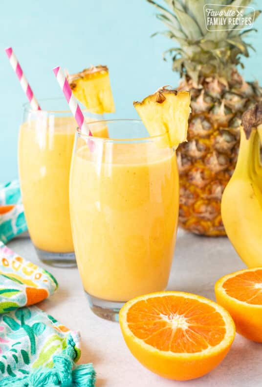 Two glasses of Tropical Banana Smoothie with straws and fresh pineapple.