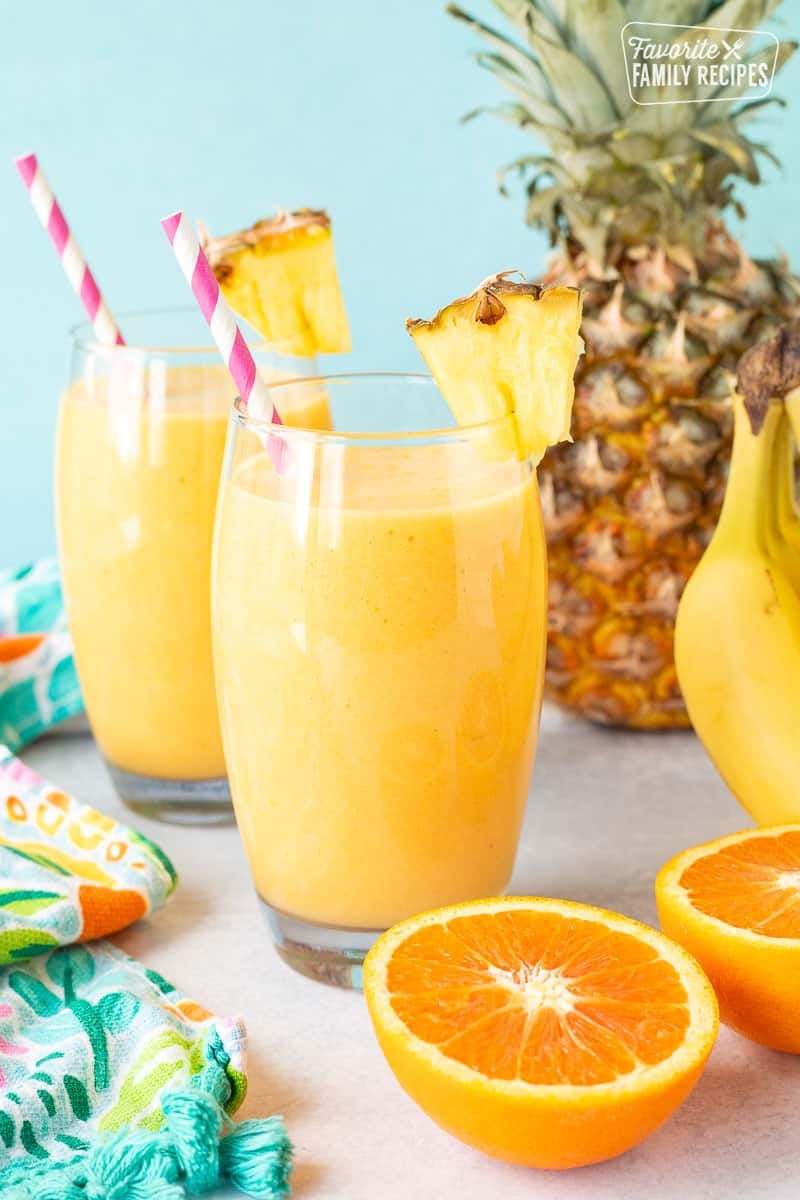 Two glasses of Tropical Banana Smoothie with straws and fresh pineapple.