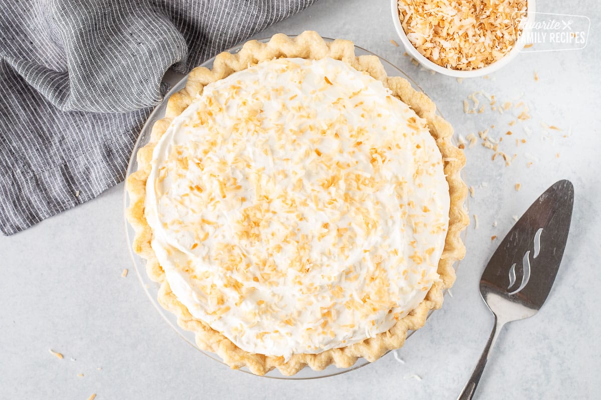 Whole Coconut Cream Pie with spatula and extra toasted coconut.
