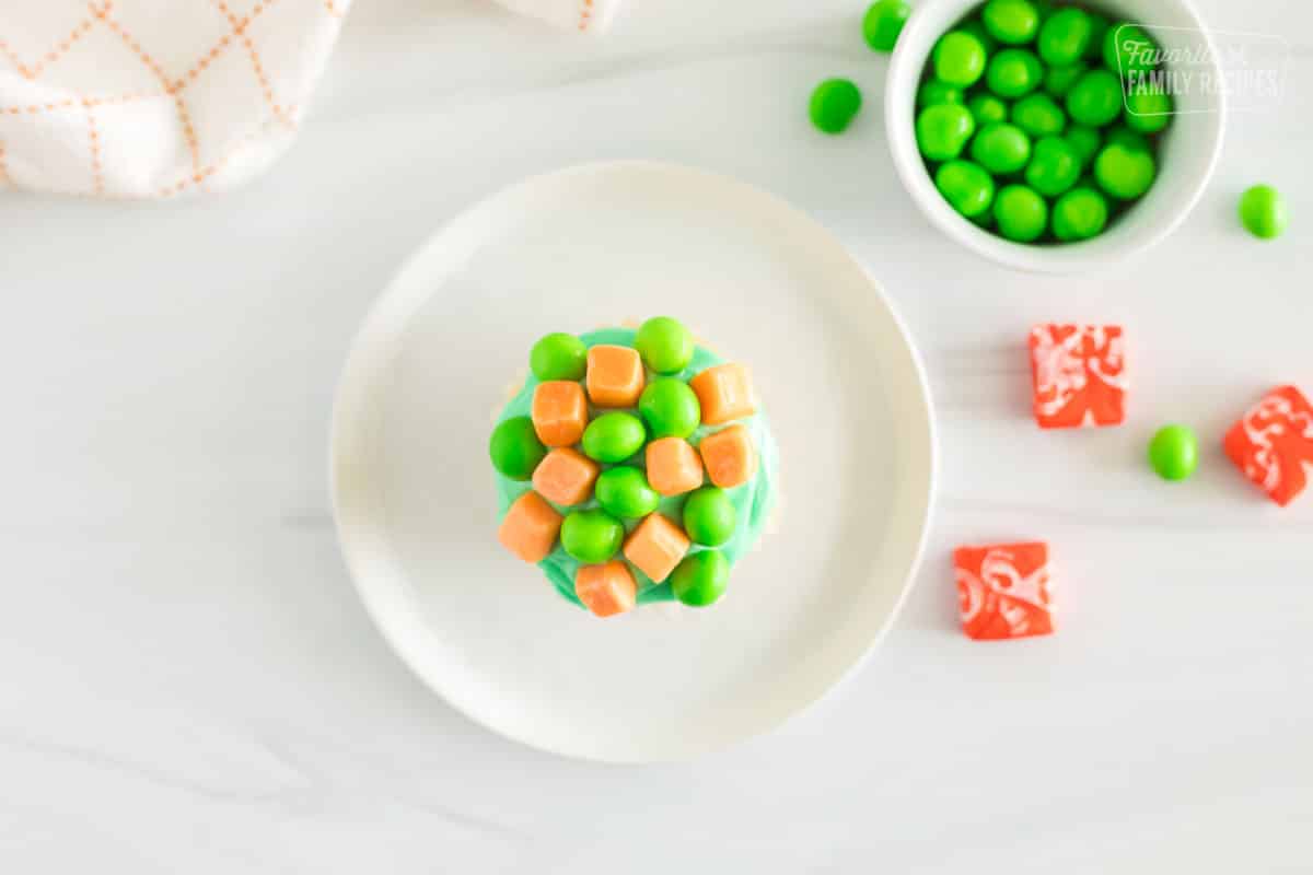 A cupcake with green frosting topped with pieces of orange starbursts and green runts