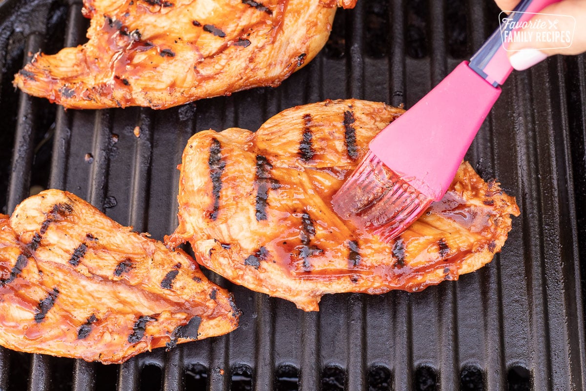 Brushing chicken breast with barbecue sauce on the grill.