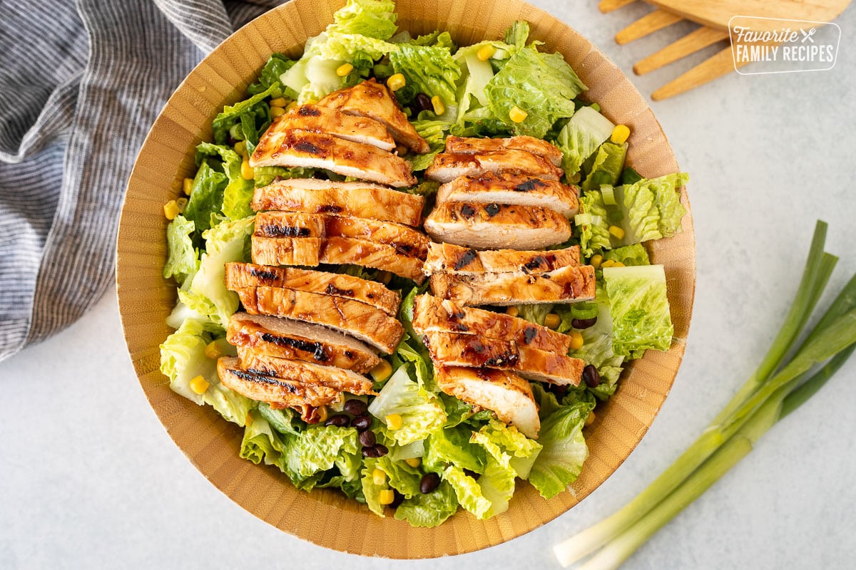 Salad bowl with sliced barbecue chicken breasts on top of romaine lettuce.