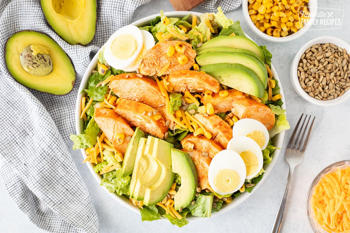 Bowl with chopped romaine salad, Buffalo chicken breasts, avocado, sliced hard boiled eggs, grilled corn, sunflower seeds and cheddar cheese.