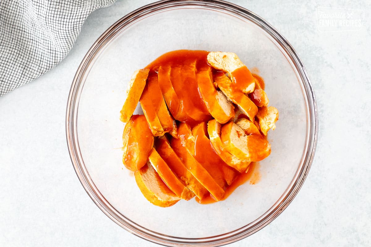 Bowl with sliced chicken breasts covered in Buffalo sauce.
