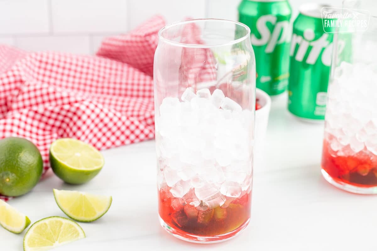Glass filled halfway with pebble ice. Cherry syrup, lime wedge and maraschino cherries on the bottom.