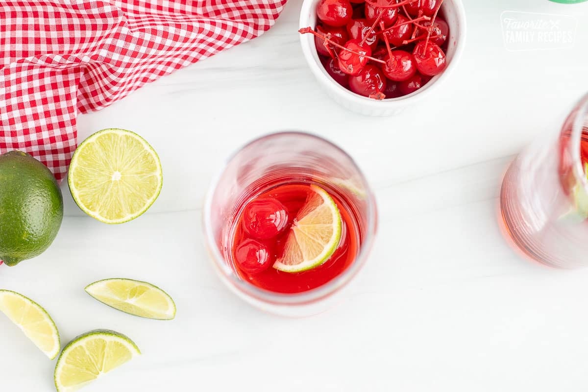 Glass with cherry syrup, lime wedge and maraschino cherries.