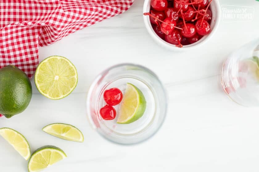 Glass with lime wedge and two maraschino cherries.