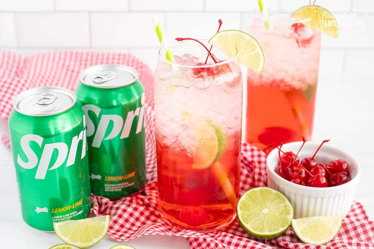 Two glasses of Cherry Limeade with two cans of sprite, limes and cherries.