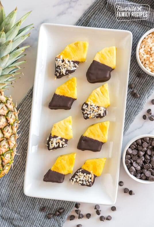Wedges of pineapple dipped in chocolate and sprinkled with toasted coconut on a platter