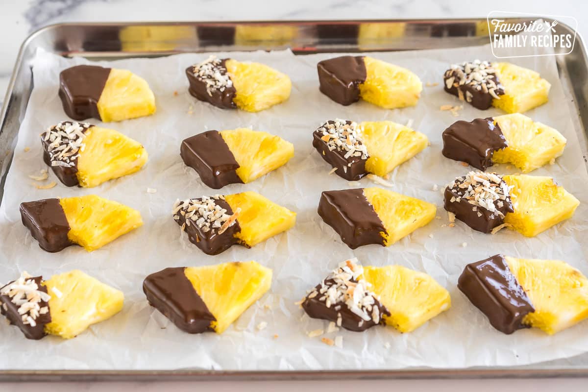 Wedges of pineapple dipped in chocolate and sprinkled with toasted coconut on baking sheet