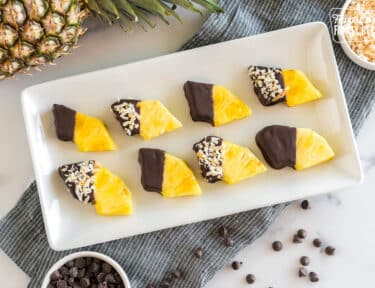 Wedges of pineapple dipped in chocolate and sprinkled with toasted coconut on a platter