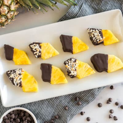 Wedges of pineapple dipped in chocolate and sprinkled with toasted coconut on a platter