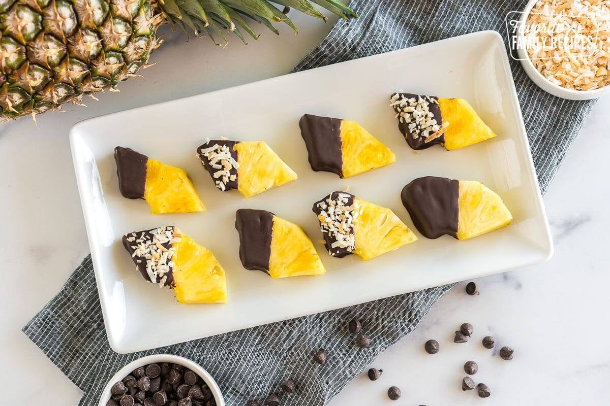Wedges of pineapple dipped in chocolate and sprinkled with toasted coconut on a platter