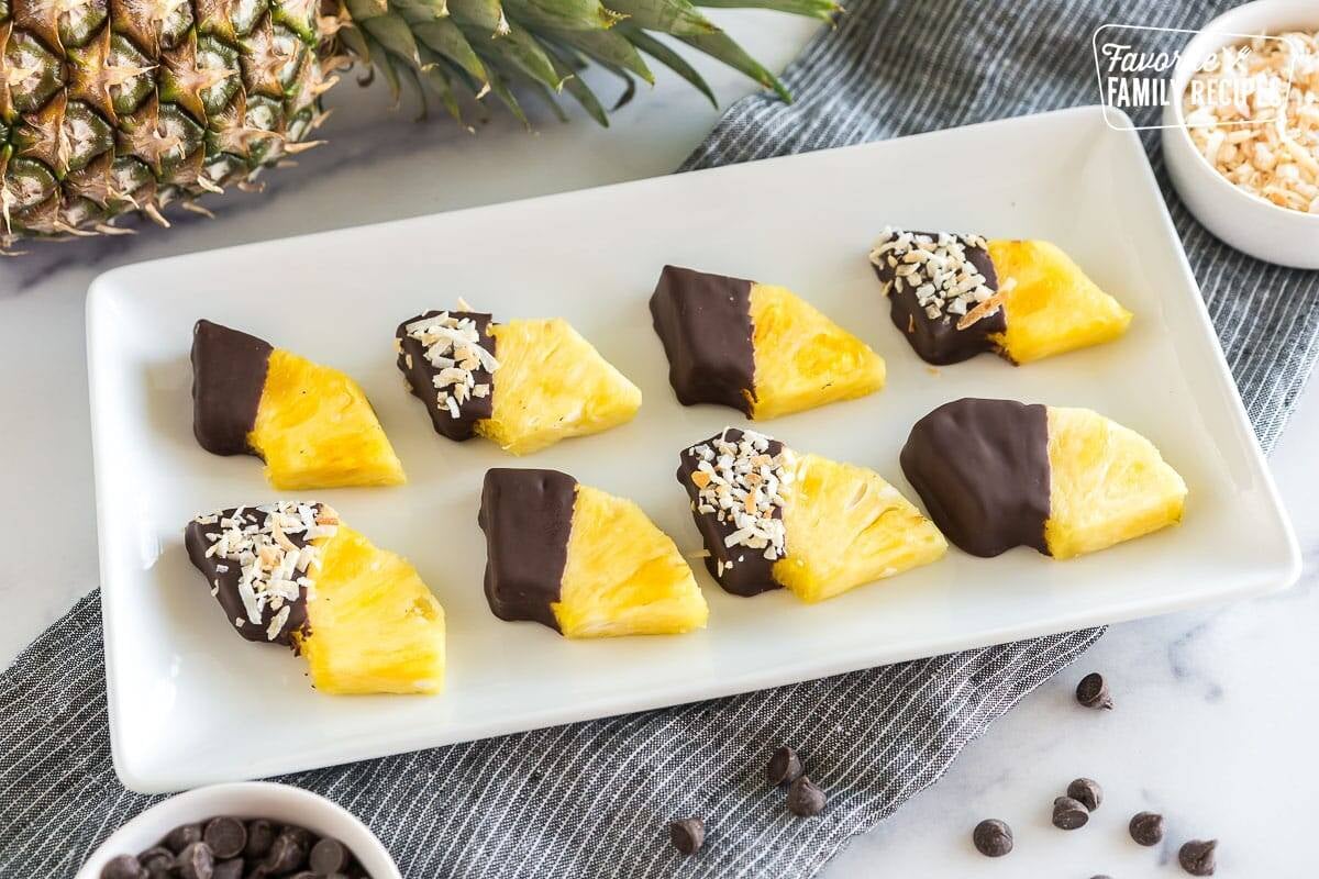 Wedges of pineapple dipped in chocolate and sprinkled with toasted coconut on a platter