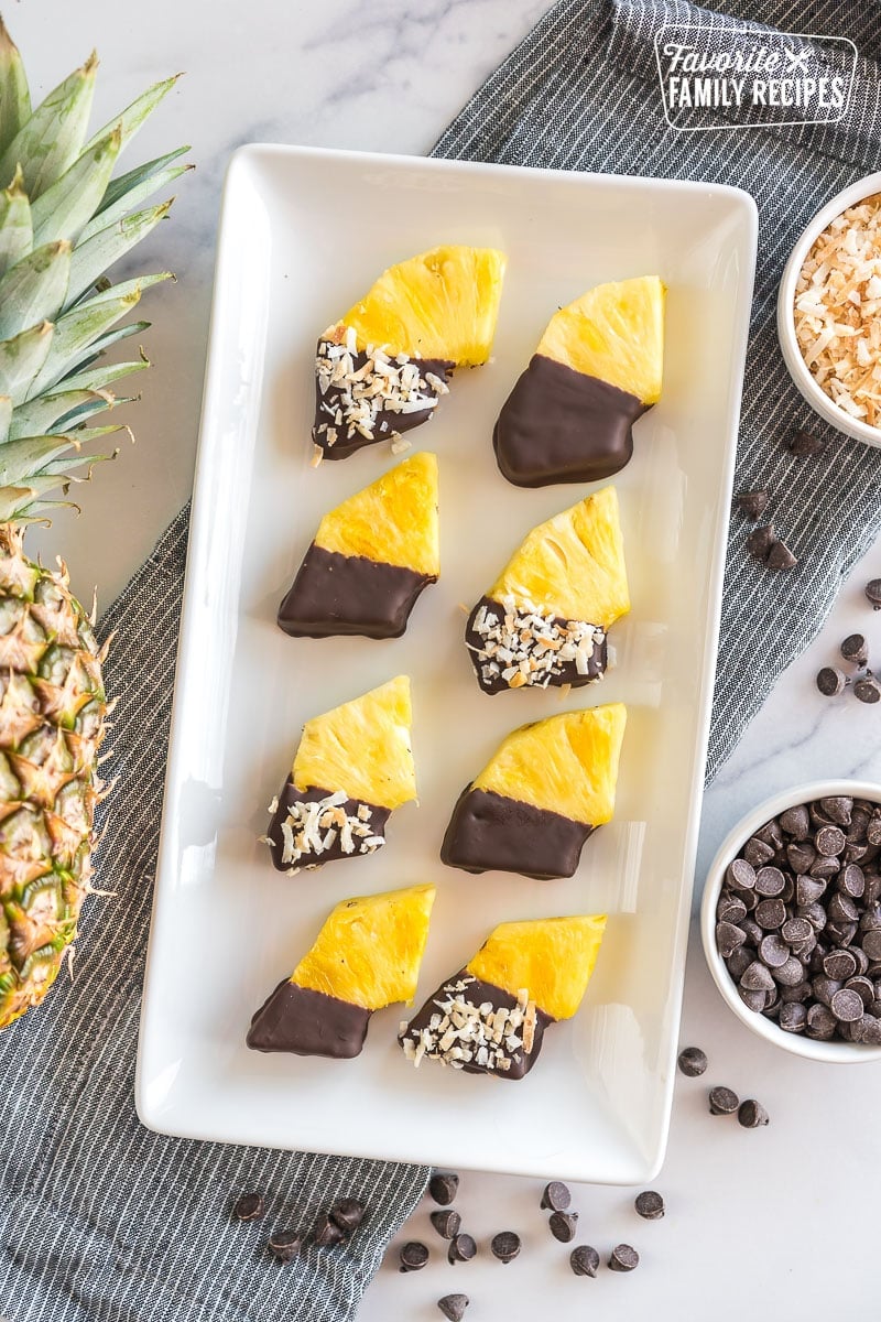 Wedges of pineapple dipped in chocolate and sprinkled with toasted coconut on a platter