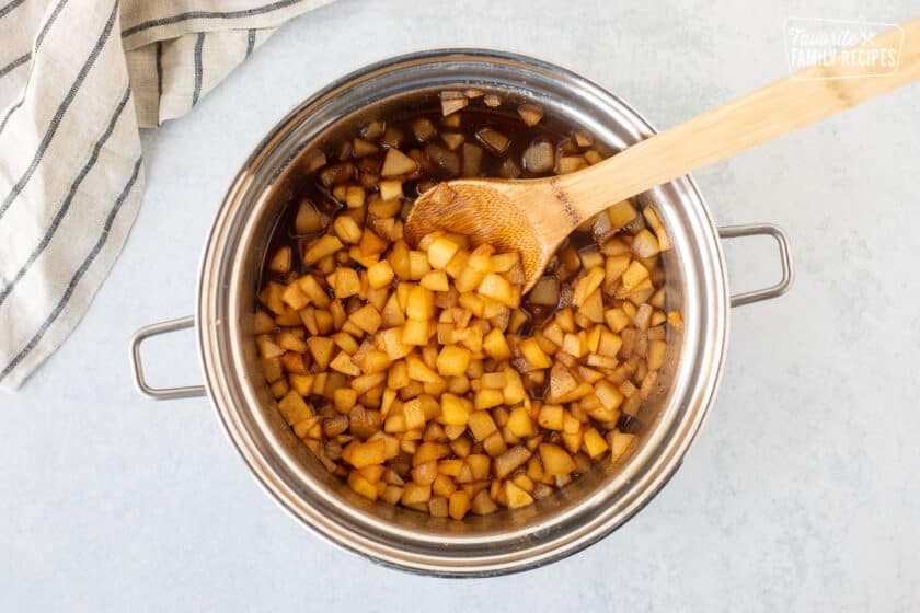 Saucepan with cooked spiced pears and wooden spoon.